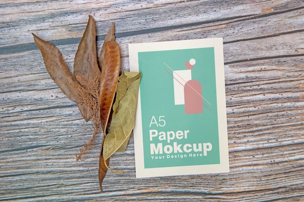 Maqueta de tarjeta de felicitación de papel A5 con hojas secas sobre fondo de madera