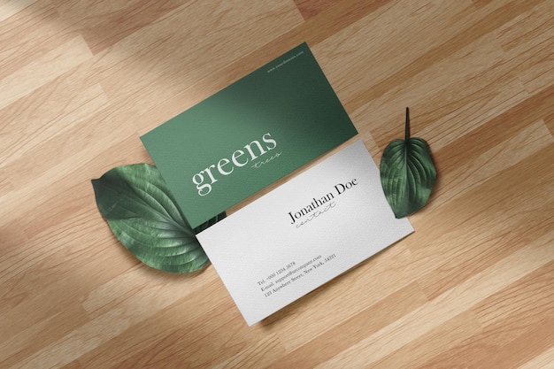 Maqueta de tarjeta de visita mínima limpia en piso de madera con hojas verdes