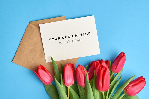 Maquete de cartão de felicitações com envelope e buquê de flores de tulipa vermelha em fundo azul