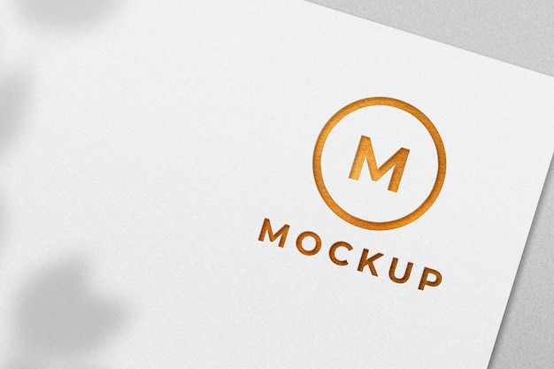 Maquete de logotipo dourado em relevo em papel branco com sombra natural