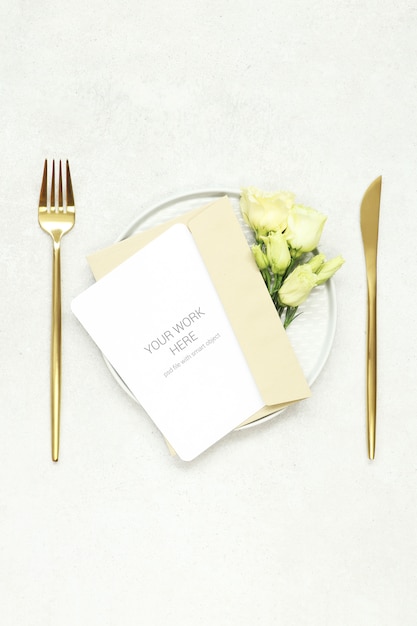 Maquette de carte d'invitation sur une assiette et des couverts en or