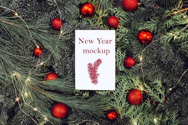 Maquette de Noël, feuille de papier blanc posé sur des branches d'épinette, boules de Noël rouges.
