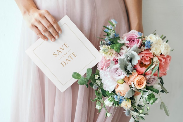 La mariée tient une maquette de carte de date avec un bouquet de fleurs