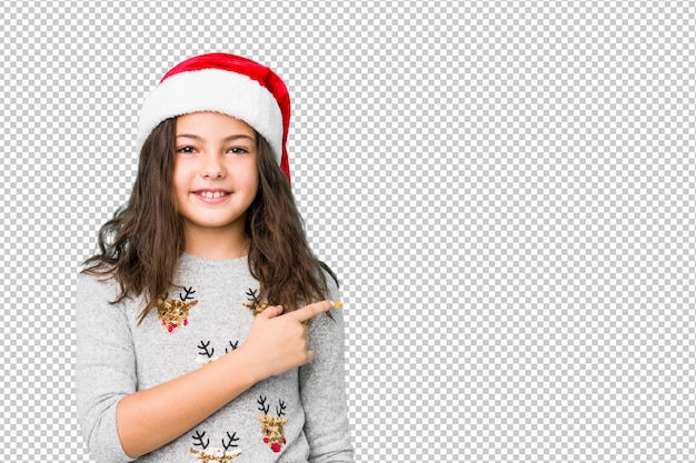 Menina comemorando o dia de natal, sorrindo e apontando de lado, mostrando algo no espaço em branco.