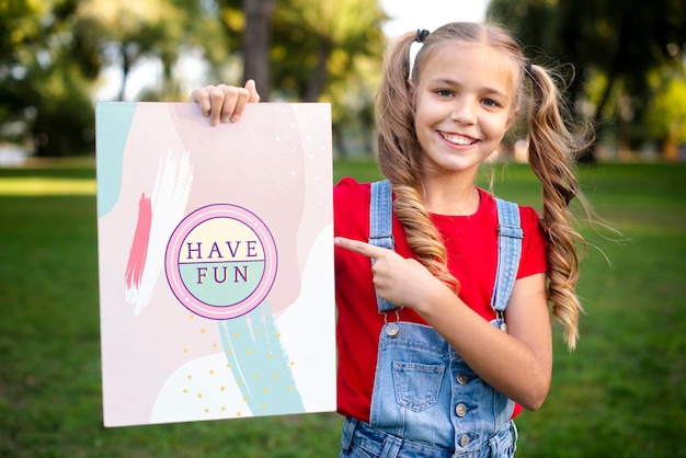 Menina sorridente com mensagem no papel, apontando para ele