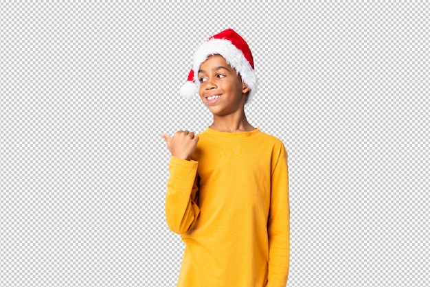 PSD menino afro-americano com chapéu de natal apontando para o lado para apresentar um produto