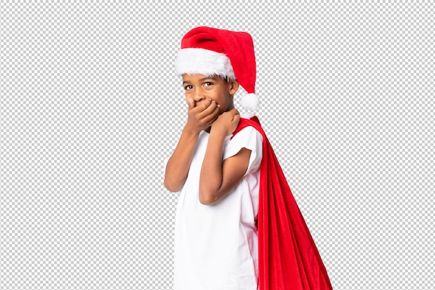 Menino afro-americano com chapéu de natal e levar uma sacola com presentes e fazendo o gesto de surpresa