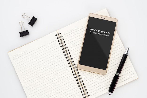 mock up blank screen of smartphone on notebook with pen on white