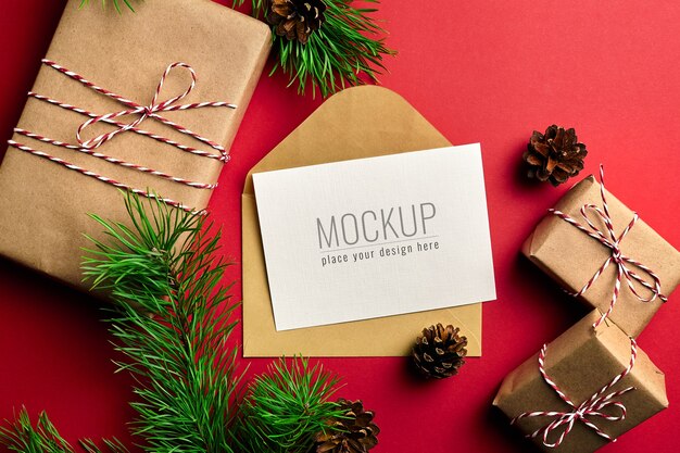 Mockup di biglietto di auguri di Natale con scatole regalo e rami di pino e coni sul rosso