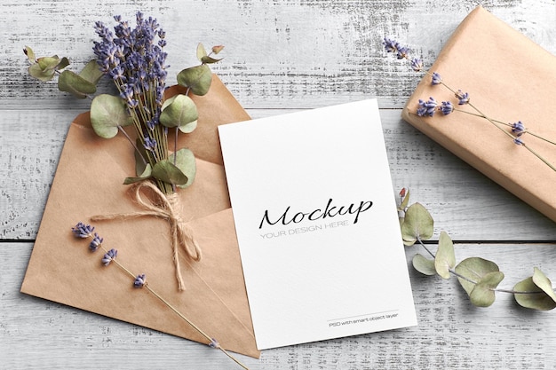 Mockup di biglietto di auguri o invito con busta, confezione regalo e bouquet di lavanda secca con eucalipto