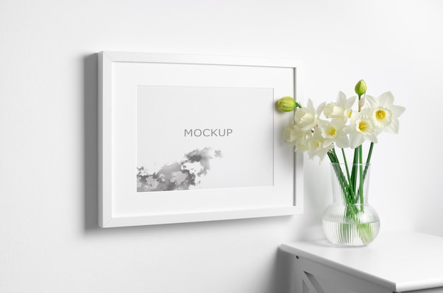 Mockup di cornice paesaggistica con fiori di narciso primaverile sul muro bianco