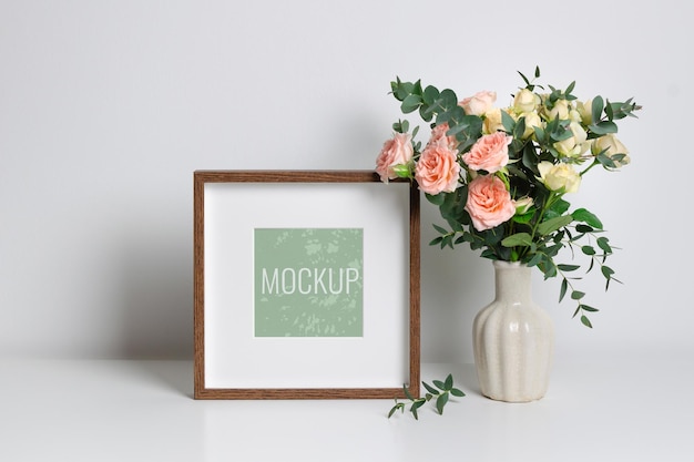 Mockup di cornice quadrata in interni bianchi con bouquet di rose in vaso