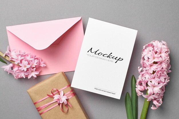 Mockup di invito o biglietto di auguri con busta rosa, confezione regalo e fiori di giacinto