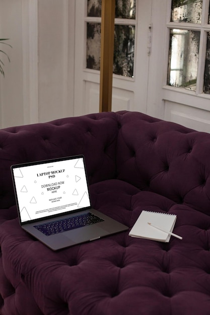 Mockup de portátil en sofá púrpura con cuaderno en el interior del hogar moderno
