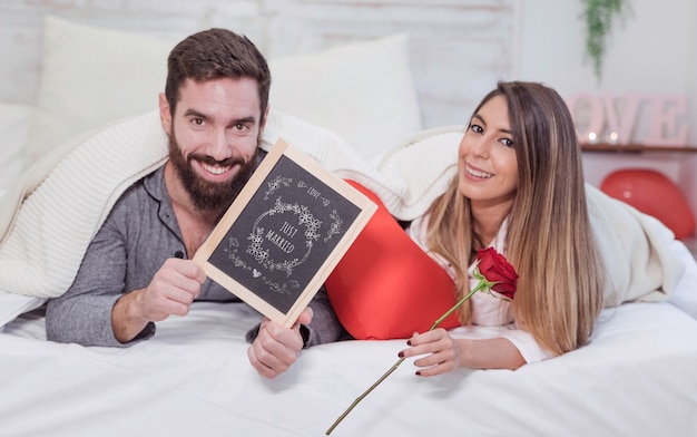 PSD mockup de san valentin con pareja en cama enseñando pizarra