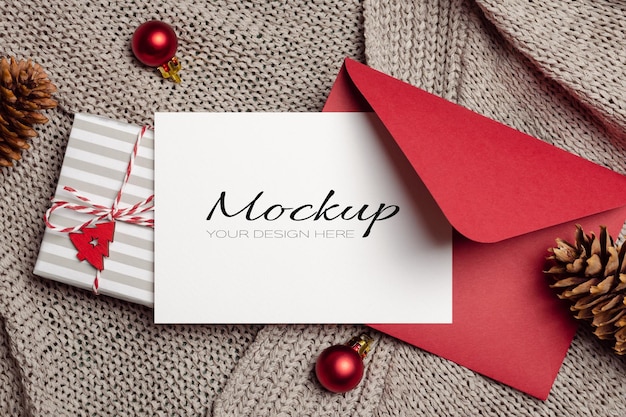 Modello di biglietto di auguri di Natale con busta regalo rossa e decorazioni festive su sfondo a maglia