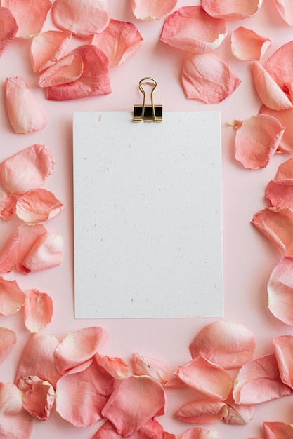 Modelo de papel clip em branco com fundo rosa claro e pétalas de rosa rosa