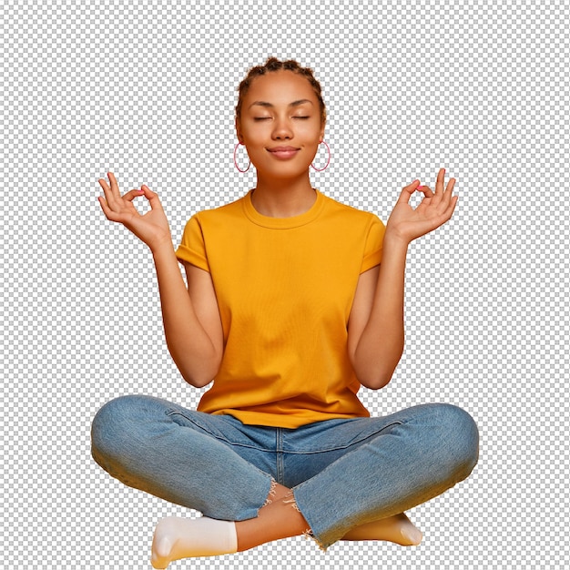 Modelo feminino de pele escura tranquila e calma senta-se com as pernas cruzadas no chão, pratica ioga e tenta relaxar, respira profundamente, fecha os olhos, alcança o nirvana, segura as mãos de lado, libera o estresse depois do trabalho.