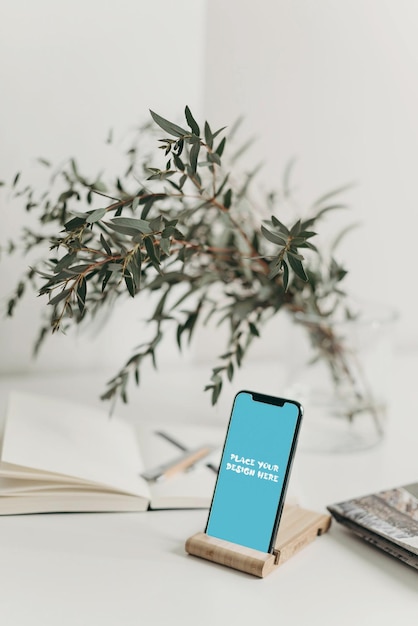 Modelo PSD editable de teléfono inteligente en soporte de madera con fondo de libro y planta