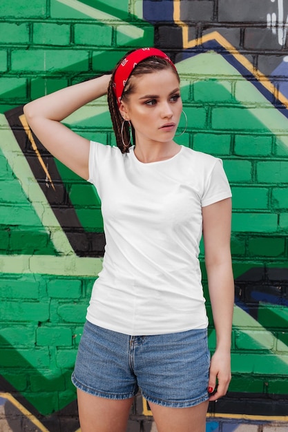 Mujer con una camiseta blanca y pantalones cortos de vaqueros frente a una pared de graffiti