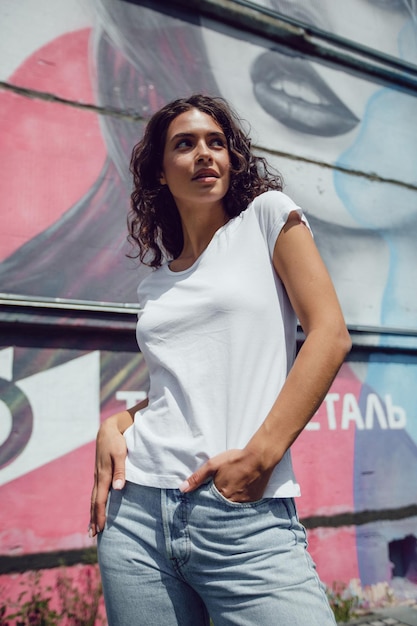 Mujer con camiseta blanca y vaqueros posando frente al graffiti