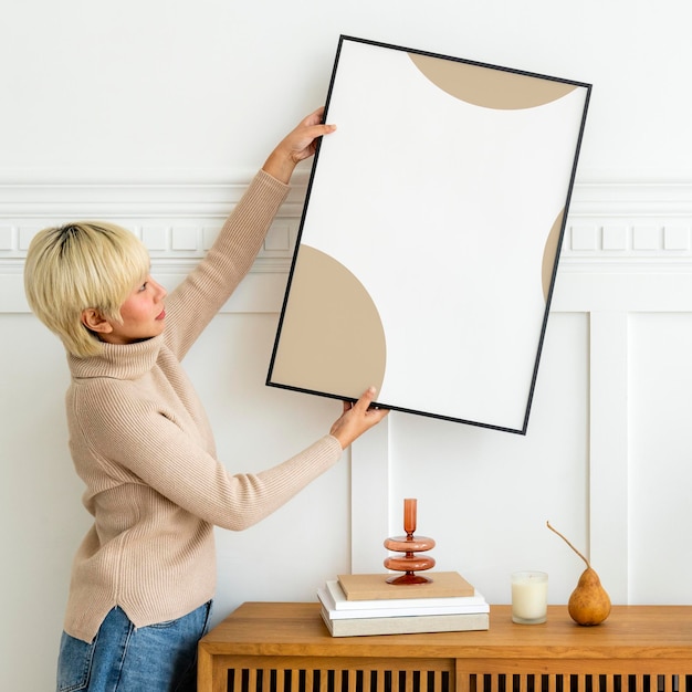 Mujer colgando un marco de fotos en una maqueta de pared blanca