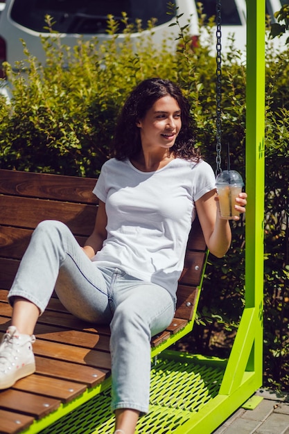 Mujer disfrutando de una bebida refrescante mientras está sentada en un columpio