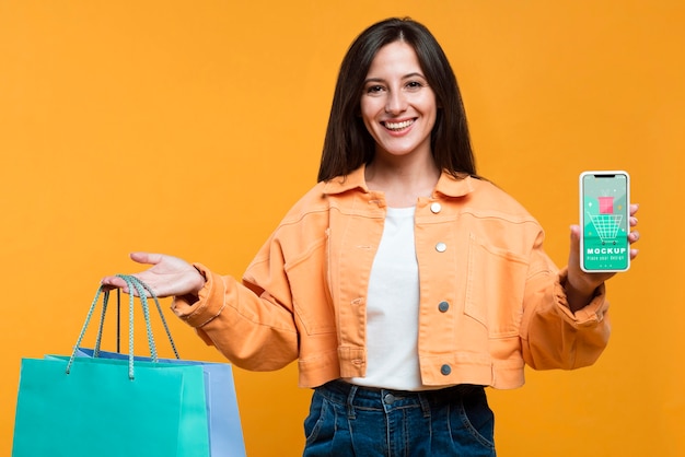 Mujer feliz sosteniendo bolsas de la compra y una maqueta de teléfono