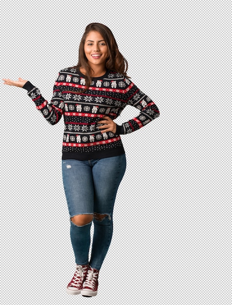 Mujer joven de cuerpo completo con un jersey de Navidad sosteniendo algo con la mano