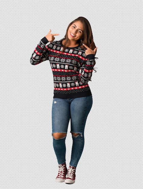 PSD mujer joven de cuerpo completo vestida con un jersey de navidad sonríe, señalando boca