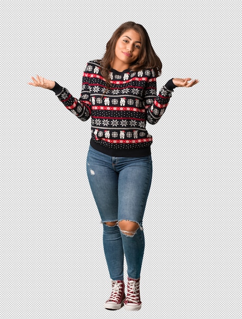 Mujer joven de cuerpo completo vistiendo un jersey de navidad dudando y encogiéndose de hombros