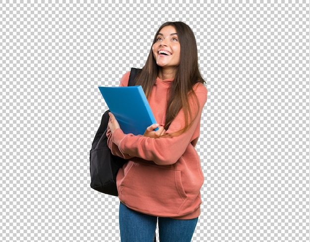 Mujer joven estudiante sosteniendo cuadernos mirando hacia arriba mientras sonríe