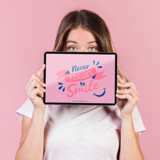 Mujer joven que cubre la cara hasta los ojos con una maqueta de tableta