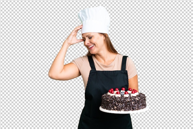 Una mujer de mediana edad, chef de pastelería, sosteniendo un gran pastel sobre un fondo aislado, sonriendo mucho.