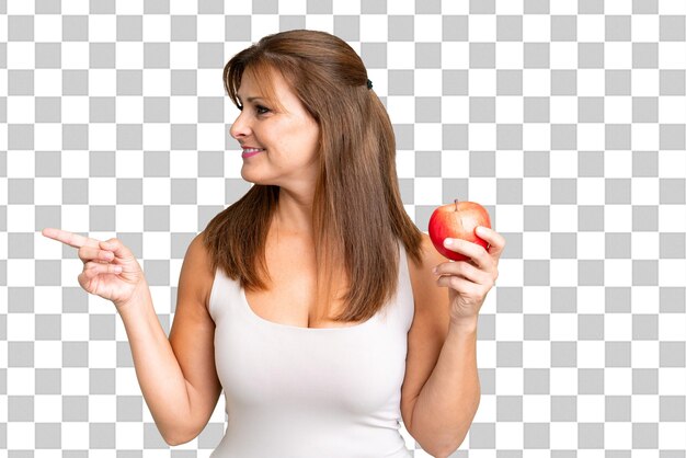 Mujer de mediana edad con una manzana sobre un fondo aislado apuntando al lado para presentar un producto