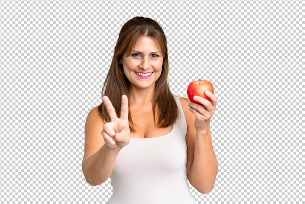 Mujer de mediana edad con una manzana sobre un fondo aislado sonriendo y mostrando el signo de la victoria