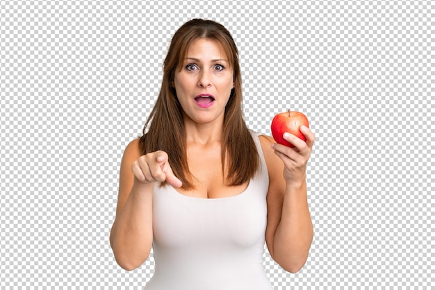 PSD mujer de mediana edad con una manzana sobre un fondo aislado sorprendida y apuntando hacia el frente