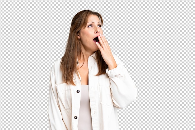 Mujer de mediana edad sobre un fondo aislado bostezando y cubriendo la boca abierta con la mano