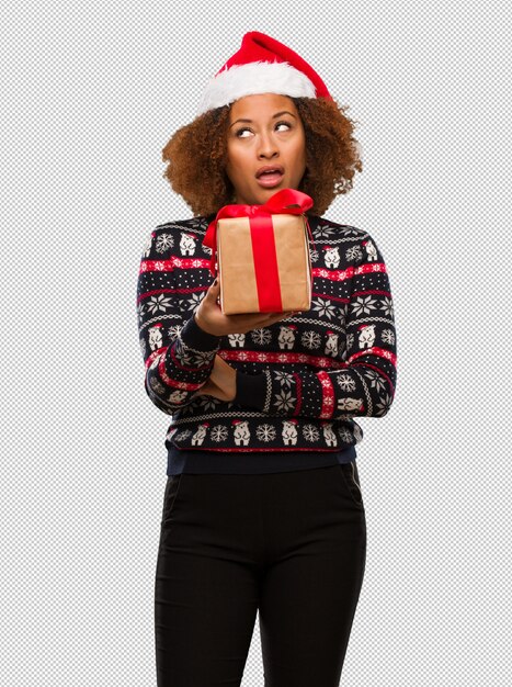 Mujer negra joven que sostiene un regalo en el día de navidad cansado y aburrido