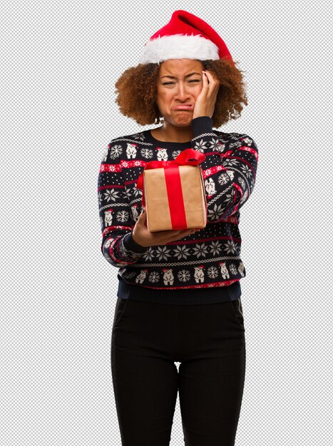 PSD mujer negra joven que sostiene un regalo en el día de navidad desesperado y triste