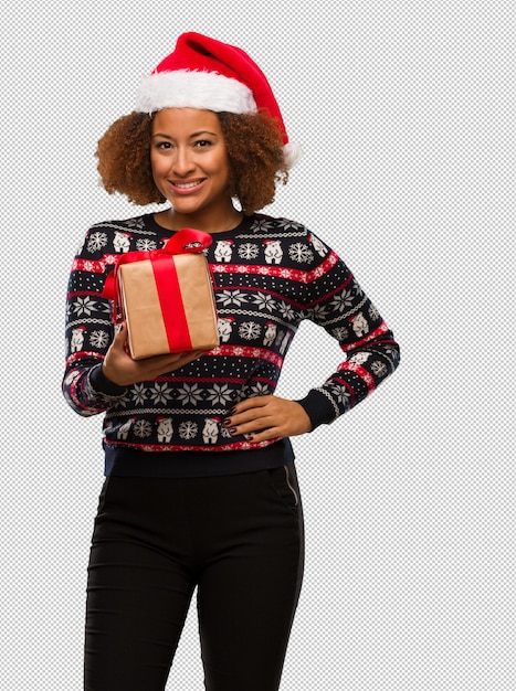 Mujer negra joven que sostiene un regalo en día de la navidad con las manos en caderas