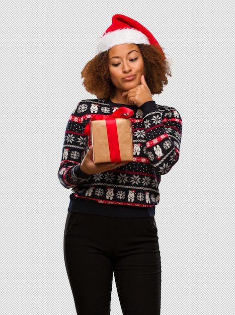 Mujer negra joven que sostiene un regalo en el día de Navidad que piensa en una idea