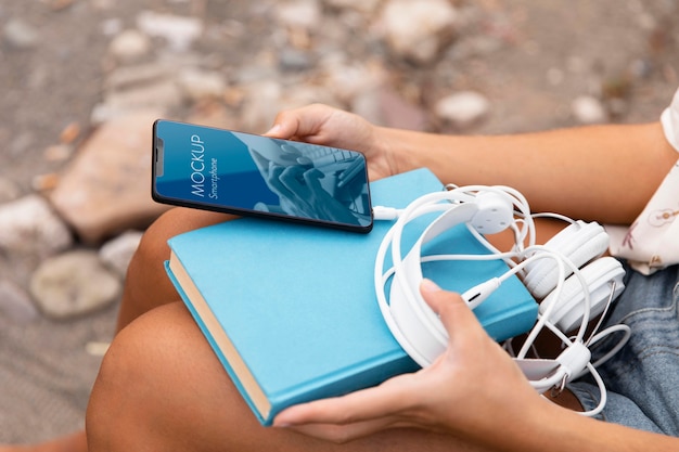 Mujer sosteniendo smartphone con libro y auriculares