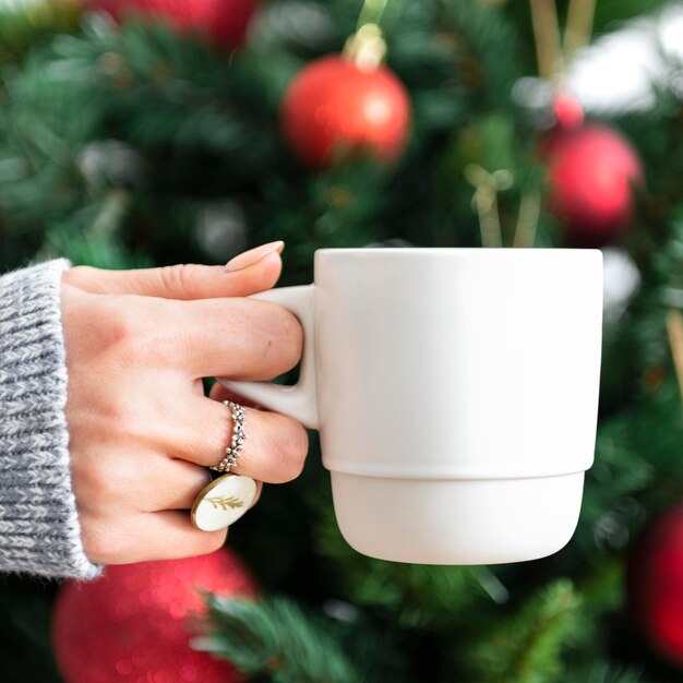 Mujer sosteniendo una taza blanca por maqueta de árbol de Navidad