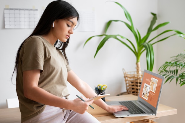 Mujer trabajando desde casa usando laptop y tomando notas