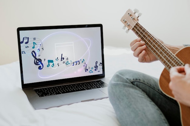 Mujer usando una maqueta de pantalla de portátil mientras toca el ukulele durante la cuarentena