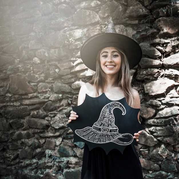 Mujer vestida de bruja sosteniendo un boceto de un sombrero