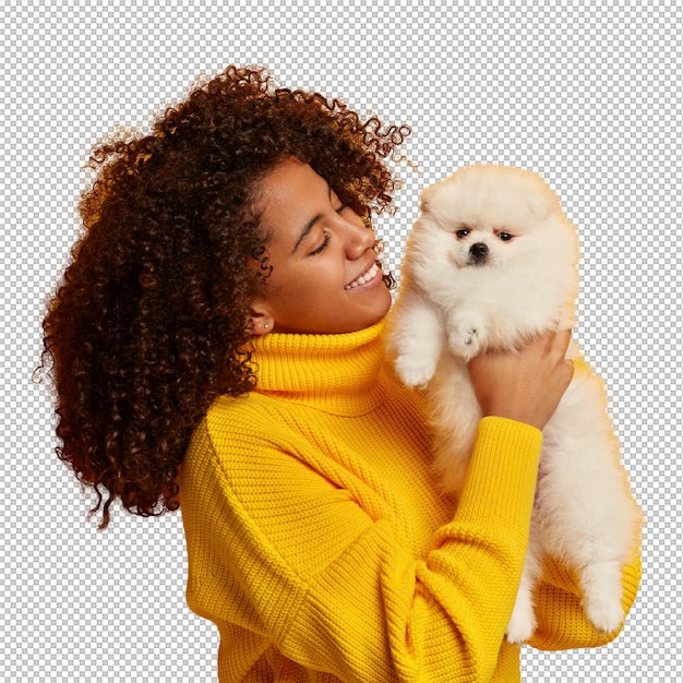 Mulher afro-americana positiva segura um cachorro em miniatura obediente nas mãos passa o dia de folga com o animal de estimação favorito comprado na loja de animais isolado sobre fundo amarelo
