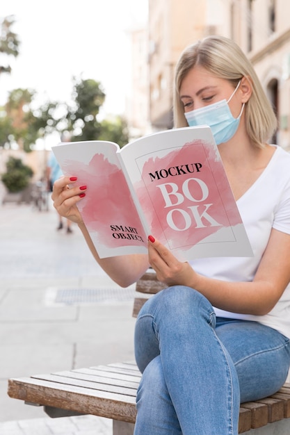 Mulher com máscara na rua lendo livro