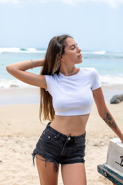 Mulher desfrutando do sol em uma praia vestindo calções curtos e um top branco